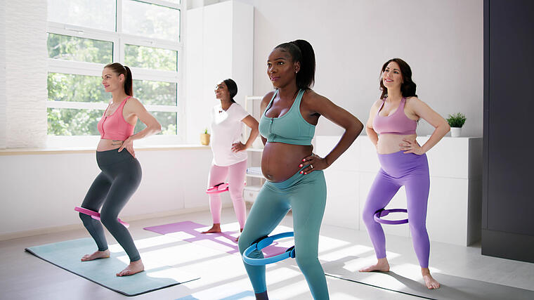 Eine Gruppe schwangerer Frauen unterschiedlicher Hautfarbe machen Yoga zusammen in einem lichtdurchfluteten Raum